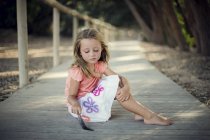Girl sitting on a wooden boardwalk and playing with feather — Stock Photo