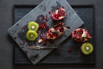 Fresh sliced pomegranate and kiwi on slate — Stock Photo