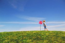 Мальчик, дующий на игрушечную ветряную мельницу, стоящую на зеленом лугу — стоковое фото