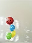 Четыре висящих в воздухе красочных воздушных шара с улыбкой на красной к серой стене — стоковое фото