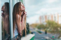 Jovem mulher inclinada para fora da janela na cidade — Fotografia de Stock