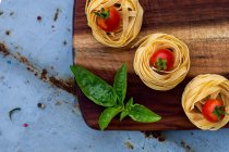 Composizione alimentare di fettuccini, pomodori e basilico su tagliere, vista dall'alto — Foto stock