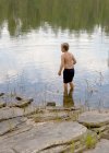Visão traseira do menino andando na água da lagoa — Fotografia de Stock