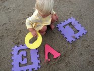Blondes kleines Mädchen spielt mit bunten Puzzle-Buchstaben — Stockfoto