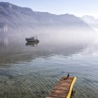Vista panoramica della barca nel lago nebbioso contro le montagne — Foto stock