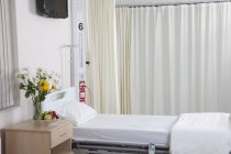 Cama de hospital vazia na enfermaria hospitalar com flores — Fotografia de Stock