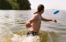 Человек играет с пластиковым летающим диском в озере — стоковое фото
