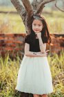 Portrait of girl wearing dress and tiara leaning against tree trunk — Stock Photo