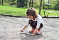 Girl drawing hopscotch on road with chalk — Stock Photo