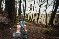 Крупним планом руки хлопчика, що висить на мотузці, що гойдається в лісі — стокове фото