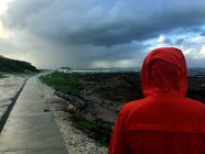 Homem vestindo jaqueta de chuva vermelha andando na costa — Fotografia de Stock