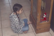 Menina sentada no chão e olhando para o duende de Natal — Fotografia de Stock