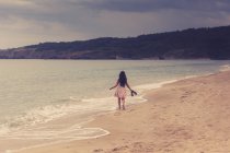 Вид сзади на девушку, идущую вдоль песчаного пляжа — стоковое фото