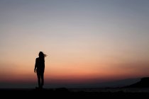 Силуэт женщины, стоящей и смотрящей на красивый закат — стоковое фото