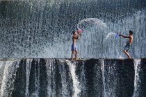 Dos chicos lanzándose agua entre sí, Tukad Unda Dam, Bali, Indonesia - foto de stock