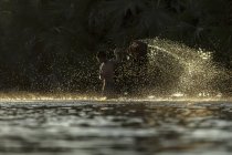 Silhouette of boy splashing water with basket in river — Stock Photo