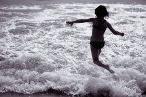 Vue arrière de la petite fille heureuse sautant dans la mer — Photo de stock