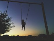 Silhouette of little boy on swing at sunset — Stock Photo