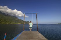 Woman sitting on swing at end of pier, Seram, Moluccas, Indonesia — Stock Photo