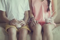 Обрізаний вид хлопчика і дівчинки, що сидить на дивані зі склянкою молока — стокове фото