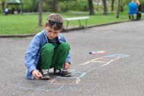Boy drawing hopscotch on road with chalk — Stock Photo