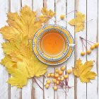 Чашка чая в окружении кленовых листьев и крабовых яблок на деревянном столе — стоковое фото