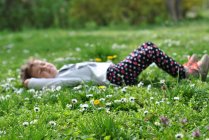 Menina deitada na grama com flor na primavera — Fotografia de Stock