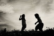 Silhouetten von zwei kleinen Mädchen, die auf einem Feld rennen — Stockfoto