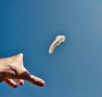 Mão humana jogando pena no ar no céu azul claro — Fotografia de Stock