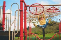 Cute little boy hanging from playground climbing frame and laughing — Stock Photo