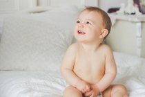Laughing baby boy sitting on bed and looking up — Stock Photo