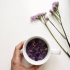 Imagen recortada de la mano sosteniendo una taza de té floral de la flor del forget-me-not - foto de stock