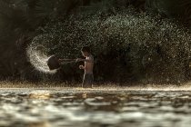 Niño sosteniendo cubo y salpicaduras en el río - foto de stock