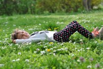 Menina deitada na grama com flores silvestres na primavera — Fotografia de Stock