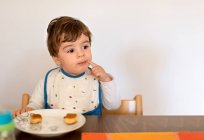 Задумливий маленький хлопчик сидить за столом їсть — стокове фото