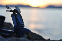 Silhouette primo piano di uno scooter parcheggiato in riva al mare — Foto stock