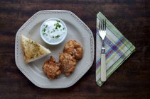 Plate of salmon cakes, dip and bread over wooden table, top view — Stock Photo