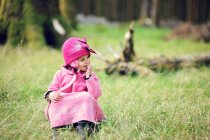 Menina vestindo casaco rosa e chapéu sentado na floresta — Fotografia de Stock