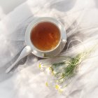 Чашка чая и маргаритки на муслине, возвышенный вид — стоковое фото