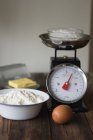 Baking ingredients on kitchen table with scales, egg and meal — Stock Photo