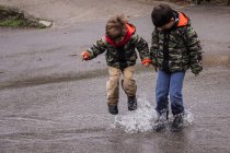 Due ragazzi caucasici che saltano in pozzanghera insieme — Foto stock