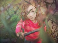 Mädchen blickt Kamera durch Äste eines Baumes — Stockfoto