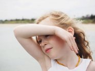 Girl with freckles shielding eyes next to lake — Stock Photo