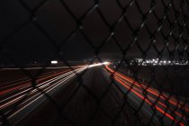USA, Indiana, Light trails at night through chain link fence — Stock Photo