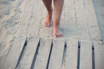 Abgeschnittenes Bild einer Frau, die barfuß am Holzdeck am Strand entlang läuft — Stockfoto