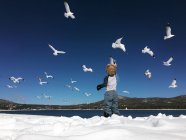Back view of little boy standing on beach in winter blowing soap bubbles at seagulls — Stock Photo