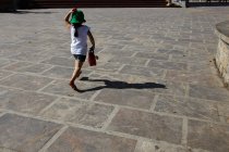 Вид сзади на девушку в шляпе, бегущую по улице — стоковое фото