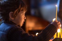 Piccolo ragazzo che tiene la candela su sfondo scuro — Foto stock