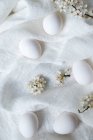 Ovos frescos e flores em tecido branco — Fotografia de Stock