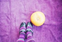Pernas em meias listradas roxas ao lado de uma abóbora — Fotografia de Stock